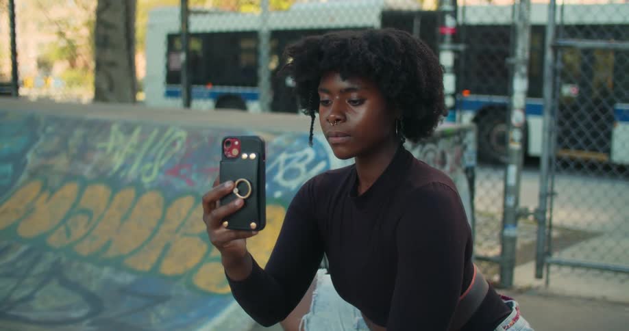 A young woman kneels with a smartphone in her hand filming or taking a selfie