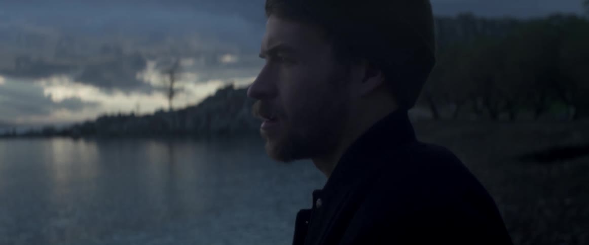 Man standing at the edge of a waterway i at a cloudy sunset