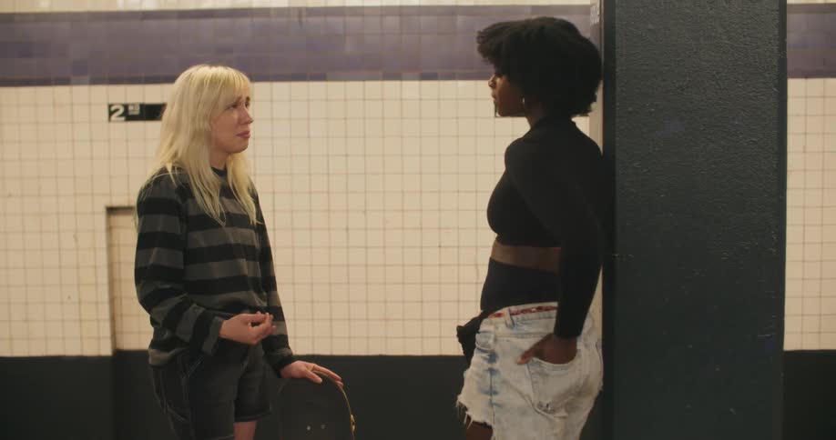 Two teenage girls stand in a subway station and have a conversation