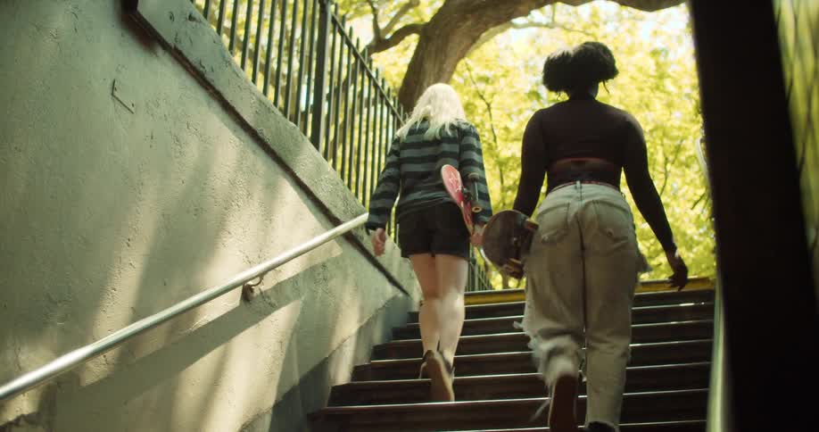 Two women walk up a flight of stairs while holding skateboards