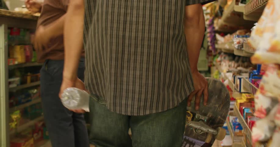 Close up of the hands of a young person carrying a skateboard while buying water on a convenience store
