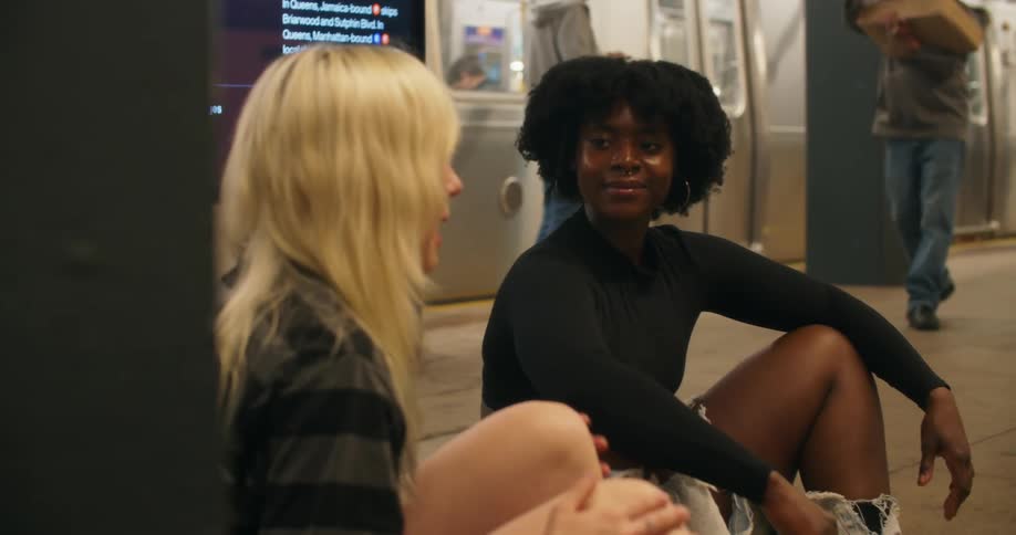 Two young teen women sitting on the floor in a subway station talking to each other