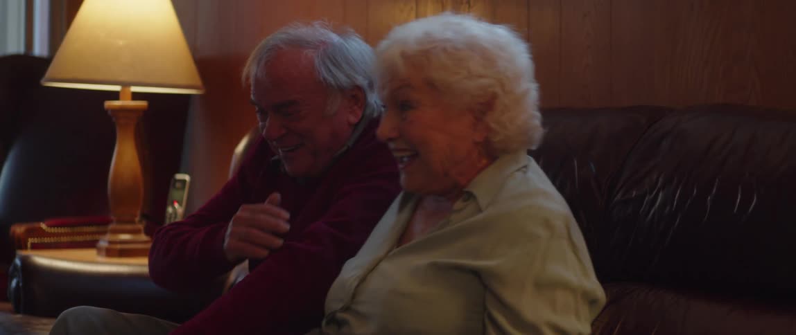 Elderly couple laughs while watching television in their living room