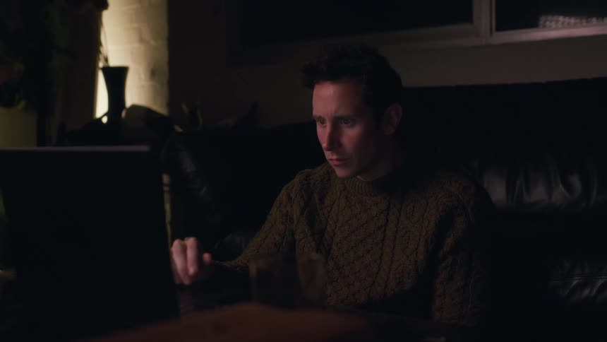 Man sitting typing on a laptop while in a dimly lit room