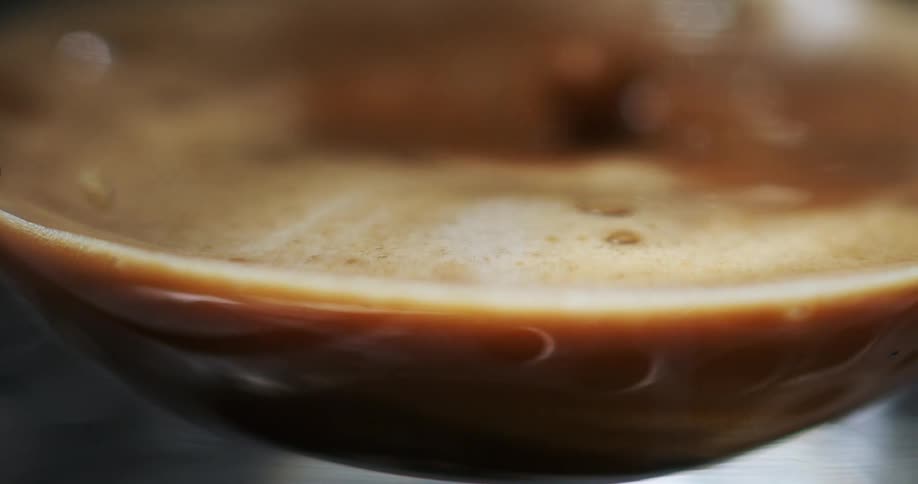A closeup view of a cup of pouring coffee with froth on top