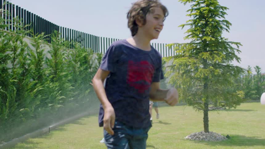 Two boys and a girl run through sprinklers in a park