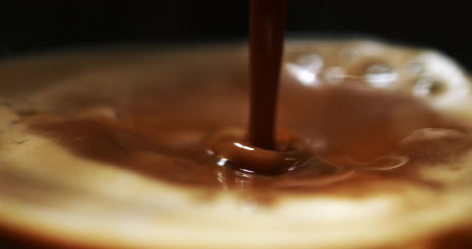 Close up of a stream of freshly pressed espresso pouring on a frothy cup