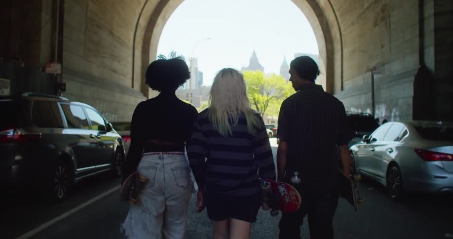 Three friends with skateboards in their hands walking down a city street