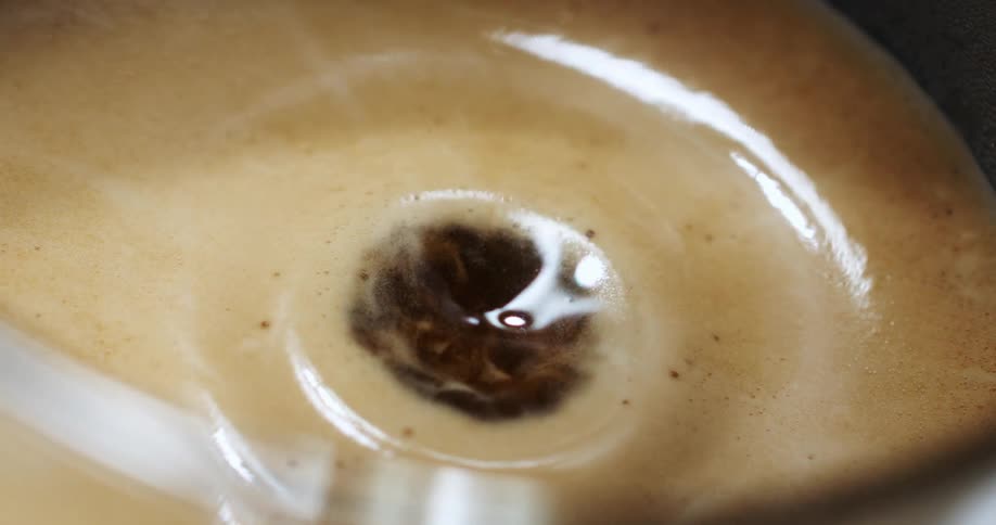 A drop of brewing coffee falls on a cup with a frothy top
