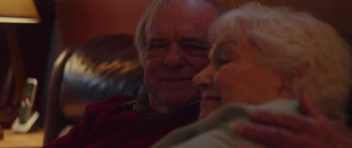 An elderly couple snuggle with each other on a couch in a living room