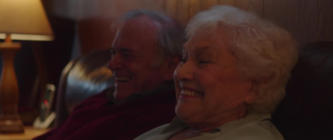 Elderly couple laughs while sitting and watching television together at home
