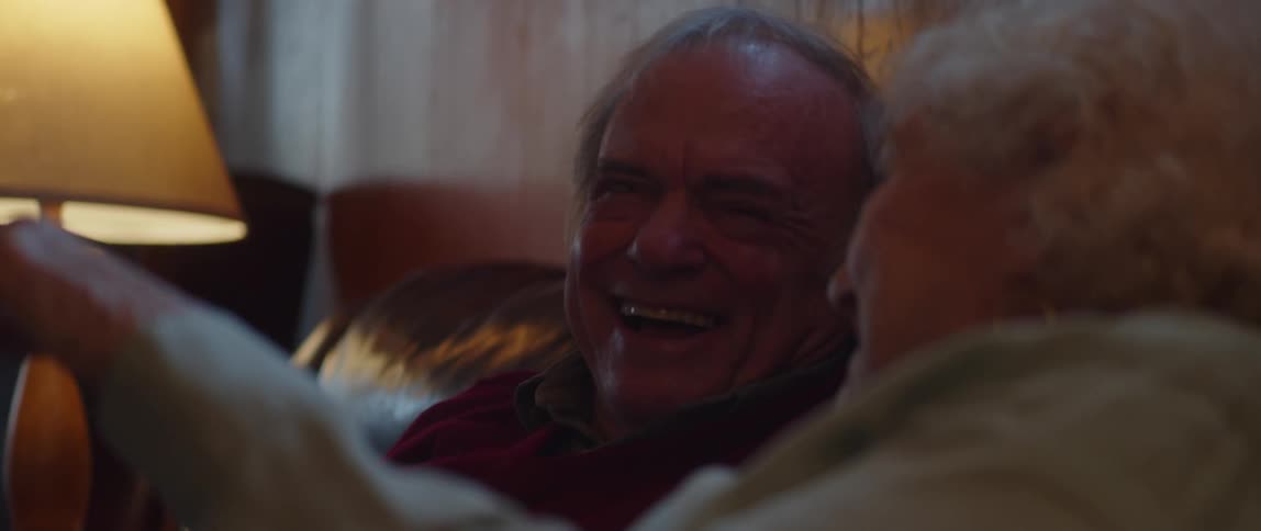 An elderly man and woman are sitting and talking while laughing at something in front of them