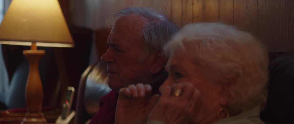 Portrait of an elderly couple sitting on a sofa watching and getting scared