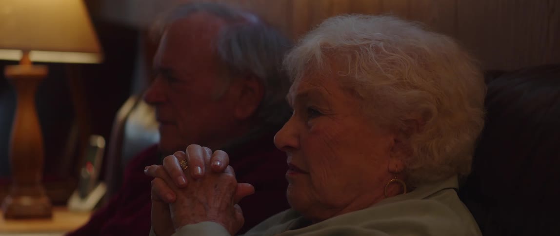 An elderly couple talking while watching television at home