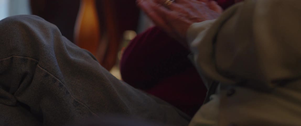 An elderly couple holds each others hands while sitting on a couch