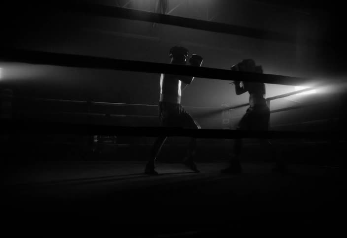 A man and a woman spar in a boxing ring as lights continuously flash