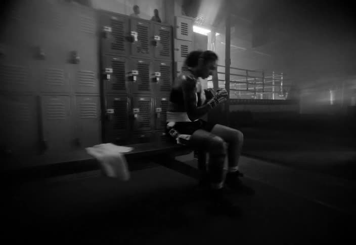A woman wearing boxing gloves boxes while sitting on a locker room bench