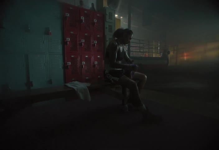A female boxer wraps her hands while sitting on a bench by lockers in a gym