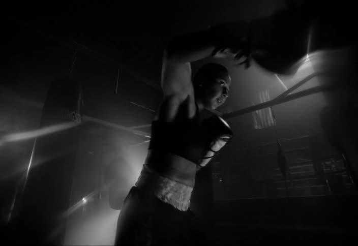 A person training in boxing and punching a punching bag and everything is in black and white