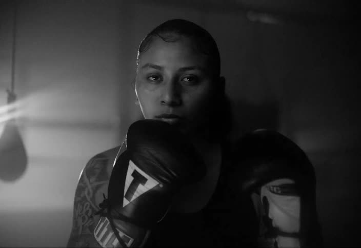Black and white close up of a female boxer looking at the camera under flashing strobing lights