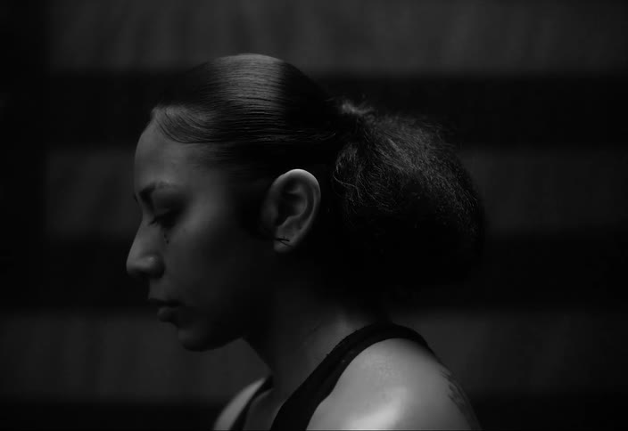 Strip of light passes over a woman standing in a dimly lit room near a flag