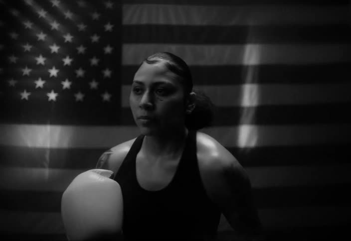 Concentrated woman warming up by throwing punches with boxing gloves with the united states flag in the background
