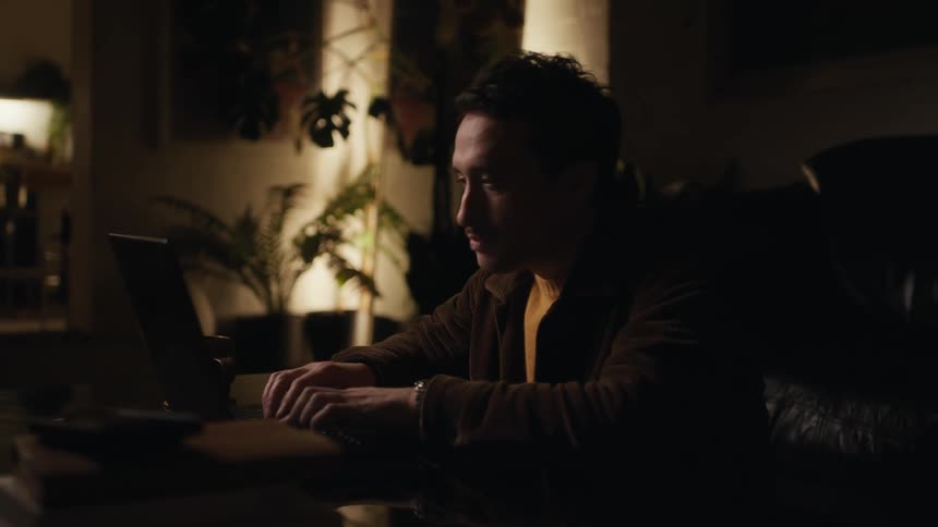 Man sitting concentrated in a dimly lit room typing on a laptop