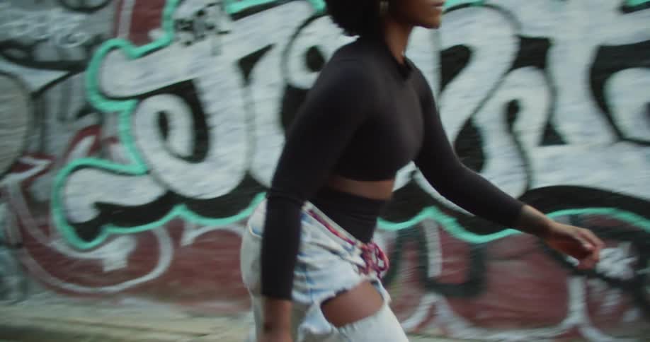 A young woman skateboards down an alleyway toward a building