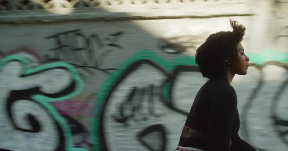 A young woman skateboarding in front of a wall covered in graffiti on a sunny day in the city