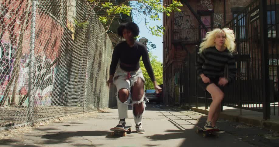 Two female friends drop their boards and start skateboarding in an alley