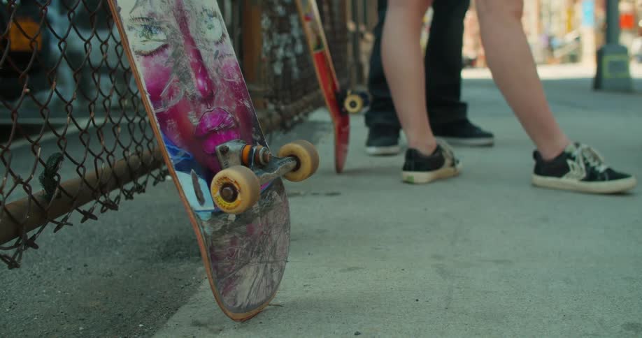 Three skateboarders stand by their boards propped up on a chain link fence in a city