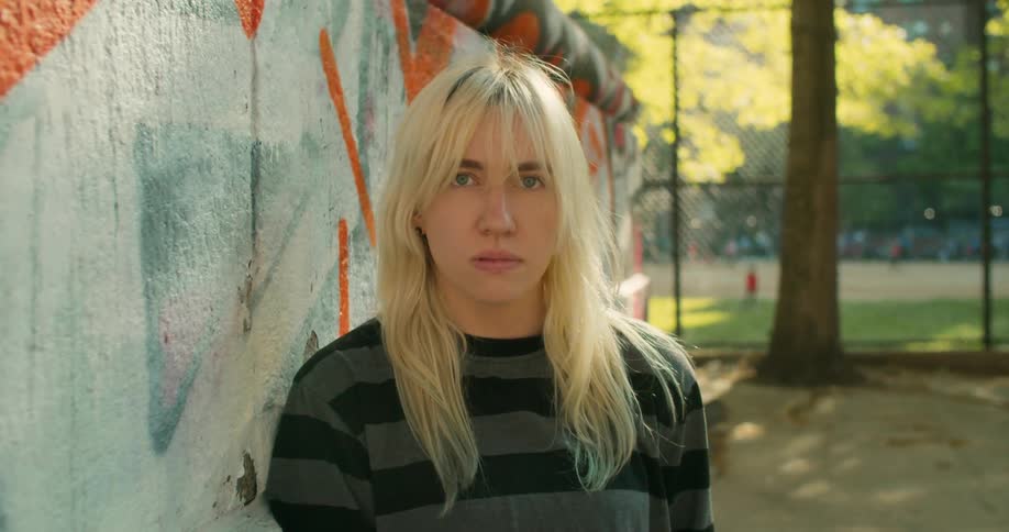A blonde female skateboarder leaning against a graffiti wall at a skate park