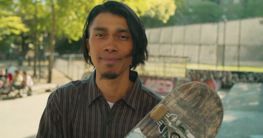 An ethnic male shows off his skateboard in a skating park