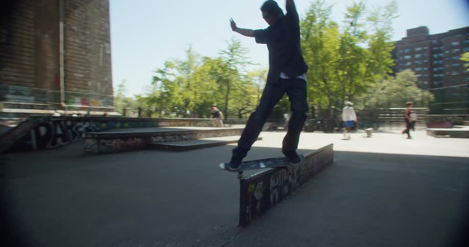 Skateboarder rides a skateboard across a low wall at a busy skate park