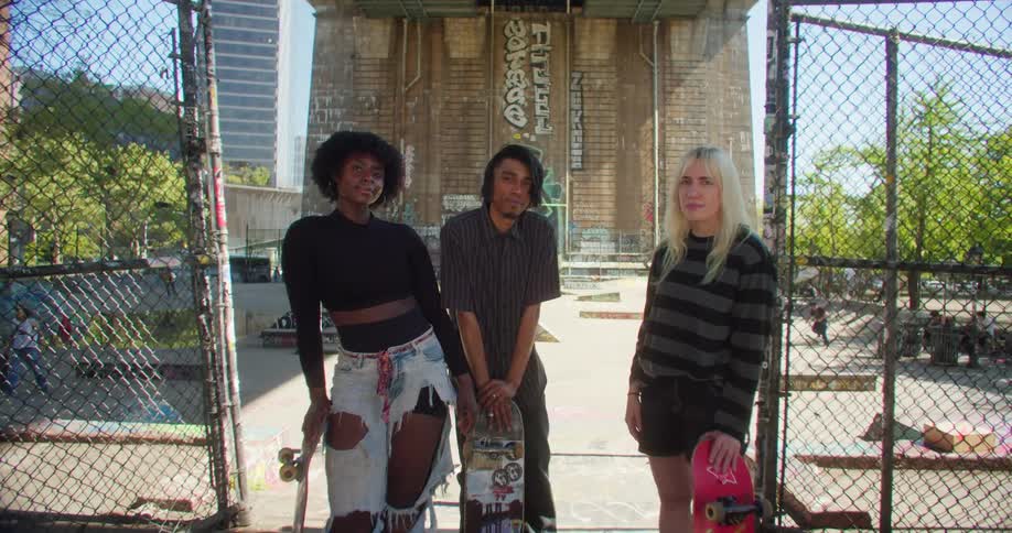 Two women and a man are standing at a skate park and holding their skateboards in front of them