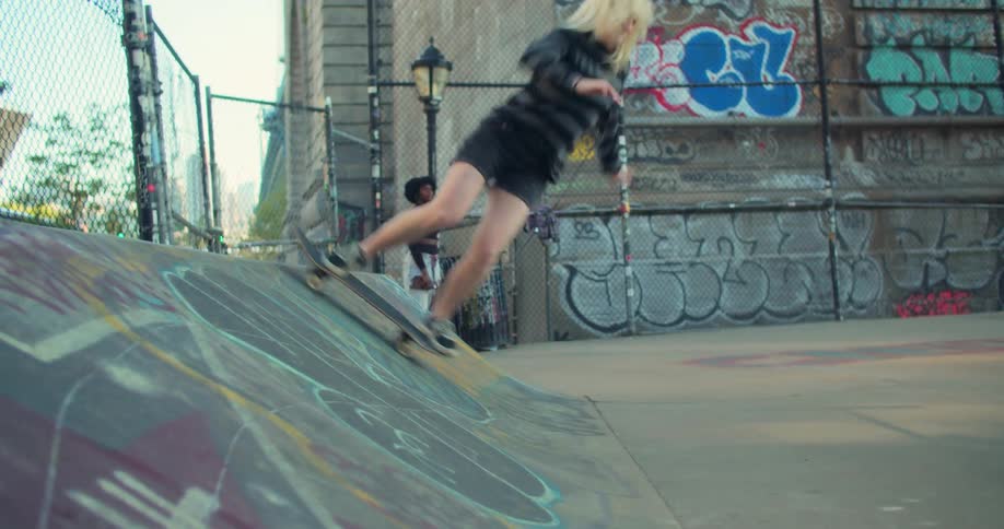 Woman rides a skateboard up a graffitied ramp and down again