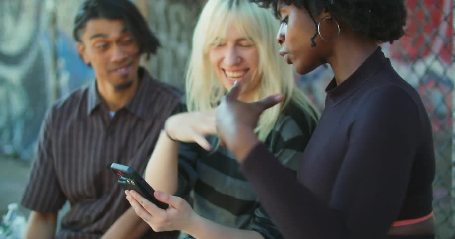 Two women and a man are looking at a cell phone and then they laugh