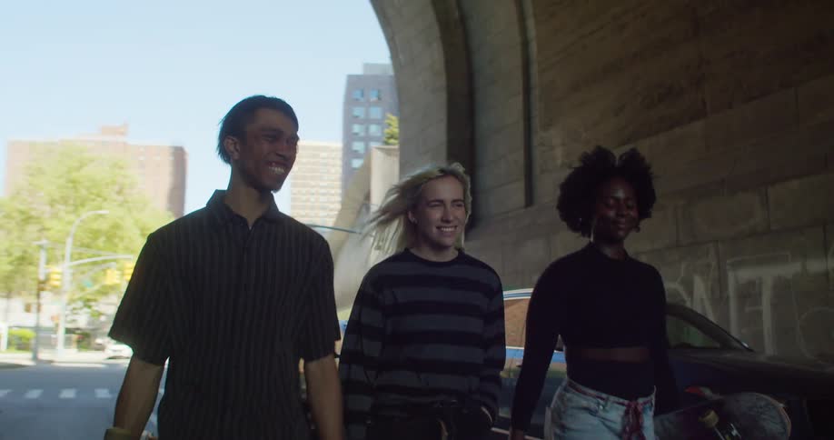 Three friends walking side by side through a city street tunnel and holding skateboards in their hands