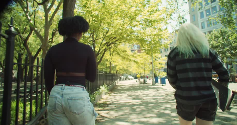 Two women leaving the subway stairs and when they reach the sidewalk they start to skateboard