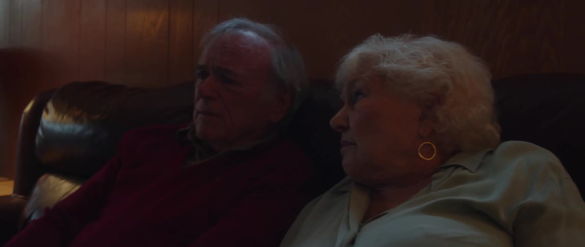 A couple watches something on tv the woman smiles and discusses the show