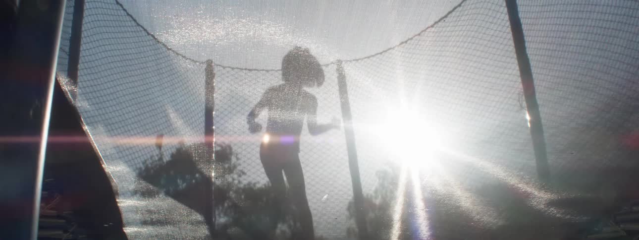 A silhouette of two children jumping on a trampoline in contrast to the bright sunlight in the sky
