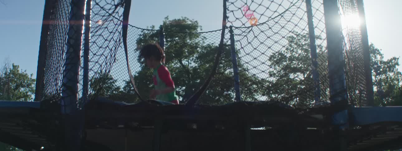 A little girl is jumping on a trampoline with safety nets and she is raising her arms up