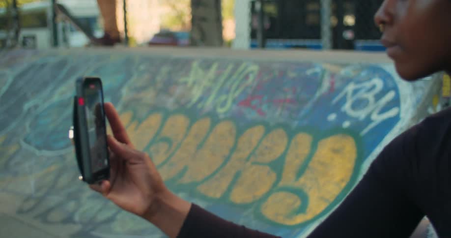 Woman sitting down filming a person doing skateboarding tricks on a ramp