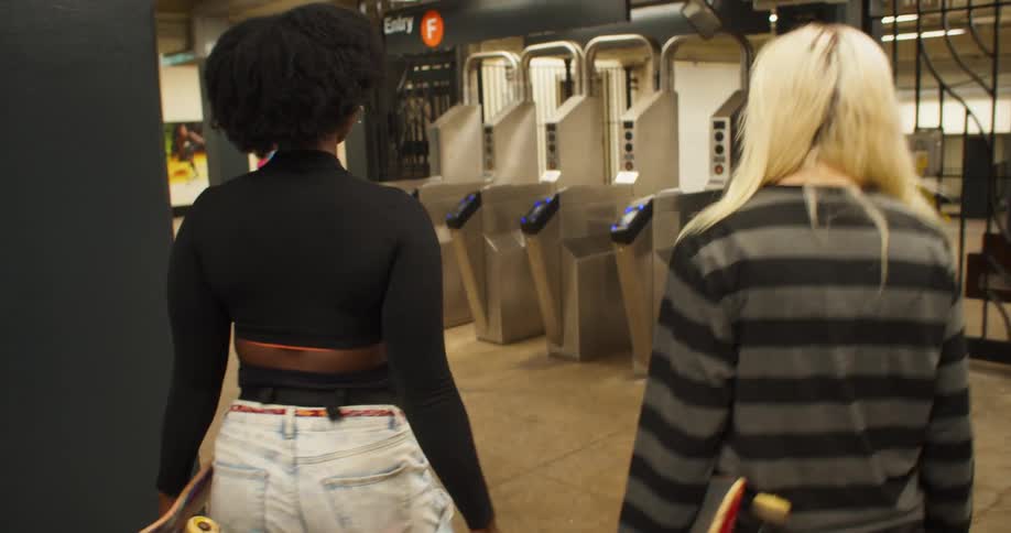 Two female friends holding skateboard in their hands walking towards a subway station