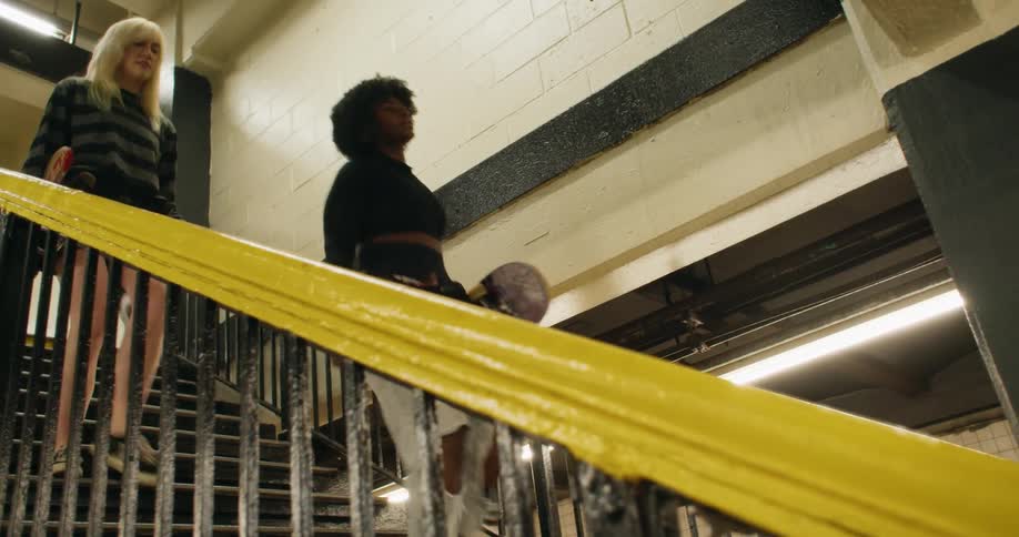 Two friends holding skateboards in their hands and going down the stairs at a train station