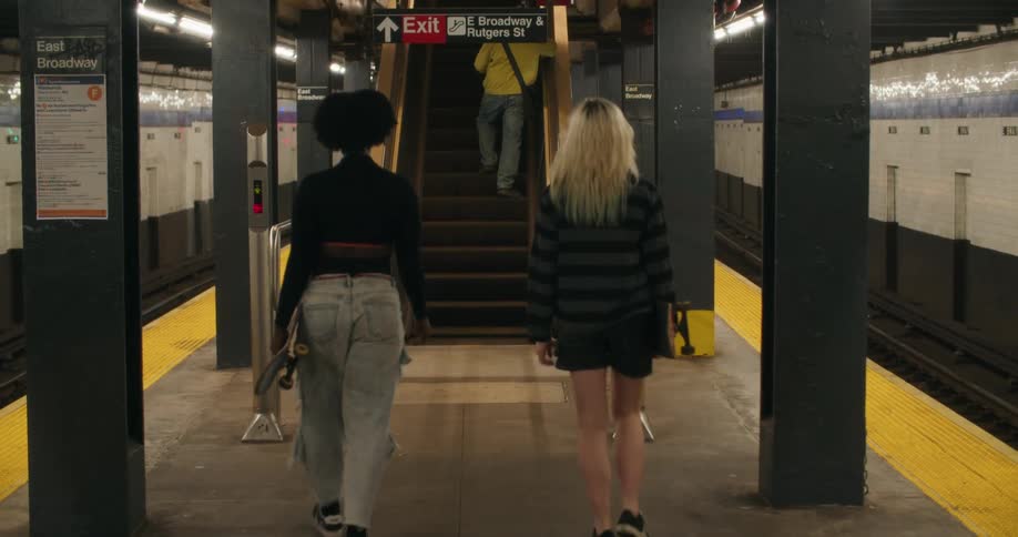 Two friends with skateboards in hand walking towards an escalator in a subway station