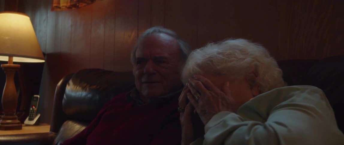 Elderly couple sitting watching a movie with a woman putting her hand on her face in a scared manner