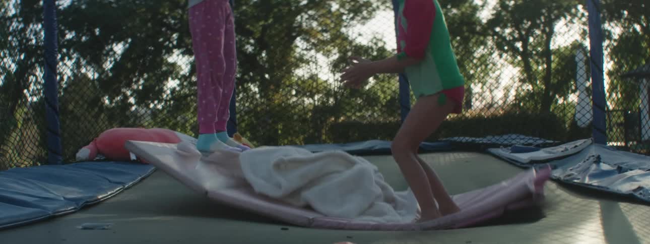 Two young girls jump up and down on a trampoline in a backyard