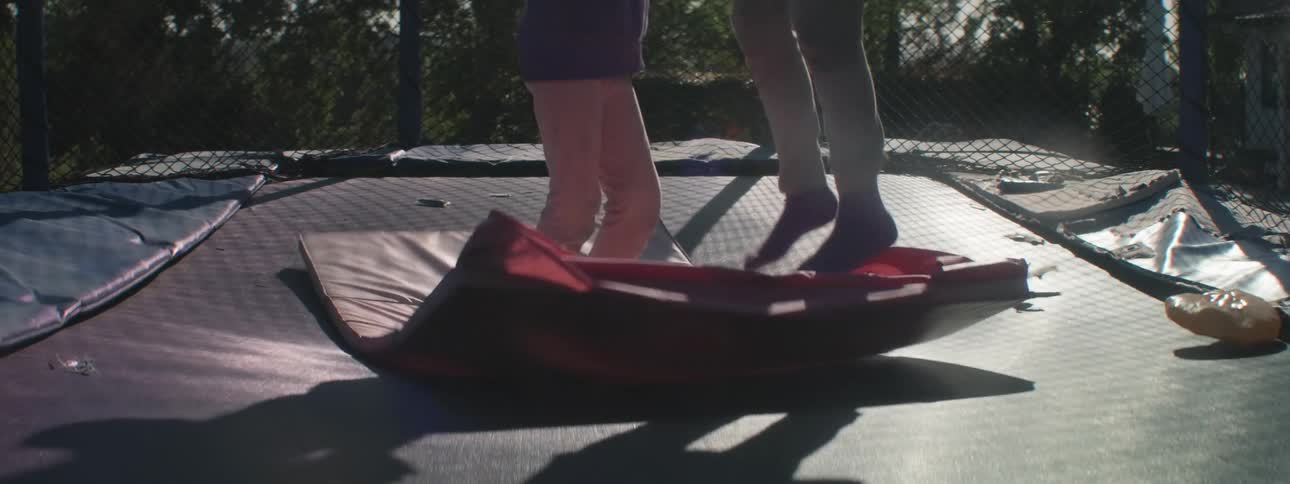 Two children jumping on a trampoline on top of a pink mattress