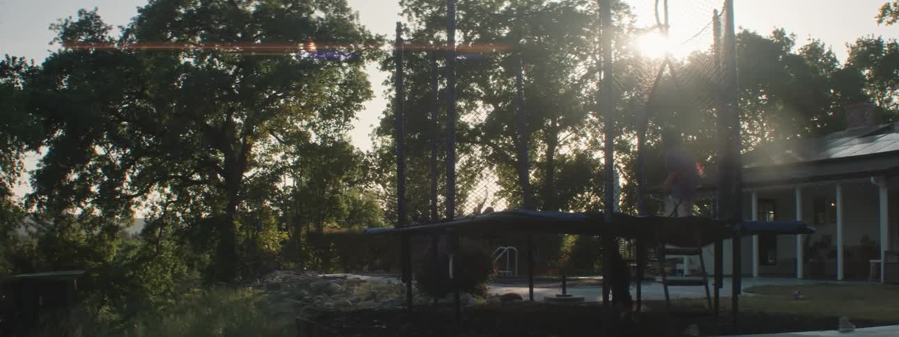 Two children jumping on a trampoline in the backyard and a dog running around